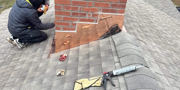 Roofers performing flashing repair around a brick chimney on an asphalt shingle roof in Connecticut